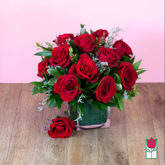 Red rose bouquet in a square glass vase on a wooden surface