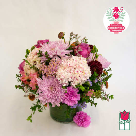 Mixed pink and purple flower arrangement in a green glass vase