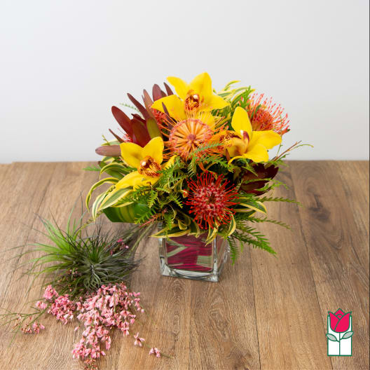 Yellow orchid bouquet in a square glass vase with pink accents