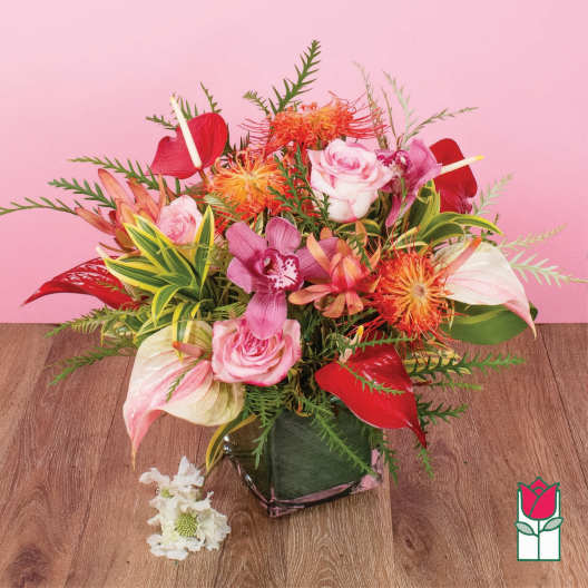 Tropical arrangement with pink roses, orchids, red anthuriums and orange blooms in a glass cube vase