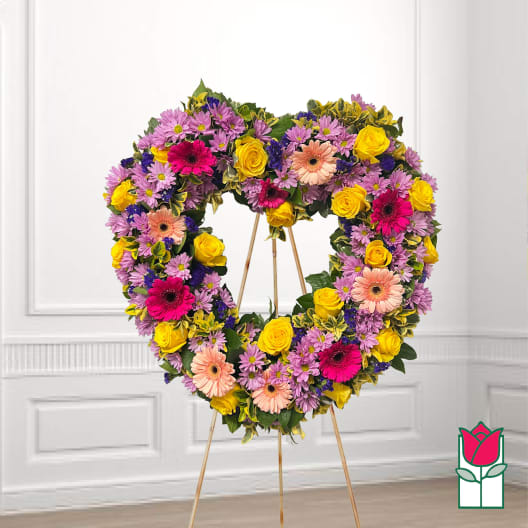 Heart-shaped floral wreath on a stand with pink, yellow, and peach blooms