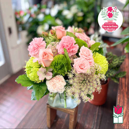 Pink roses and carnations arranged in a glass vase with bright green blooms
