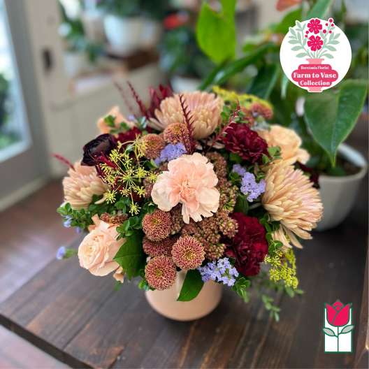 Mixed bouquet of peach, burgundy, and lavender flowers in a pale vase