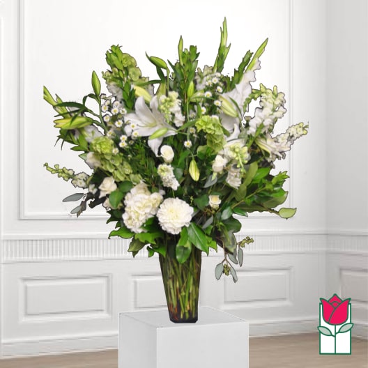 White lilies and mixed white flowers in a tall glass vase