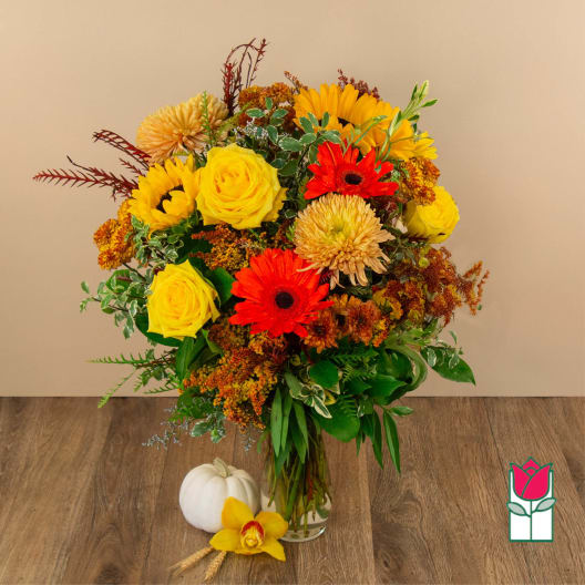 Bright mixed bouquet with yellow roses, red gerberas, and sunflowers in a glass vase