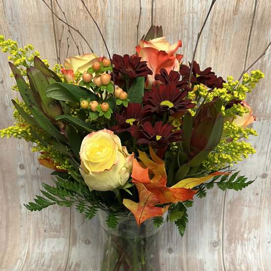 Bouquet of cream and orange roses with dark burgundy daisies in a glass vase