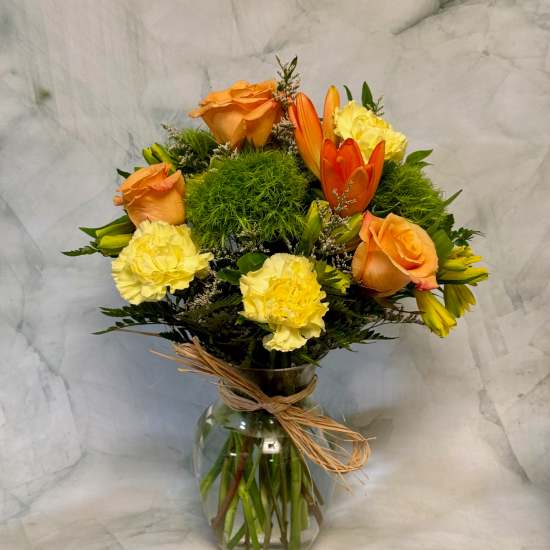 Orange roses and yellow carnations in a glass vase with raffia tie