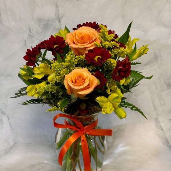 Bouquet of peach roses, red daisies, and yellow flowers in a glass vase