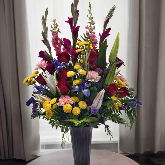 Tall mixed bouquet of roses, lilies, and colorful filler flowers in a purple vase