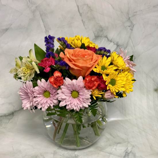 Mixed bouquet in a clear glass vase with an orange rose, daisies, and colorful filler flowers