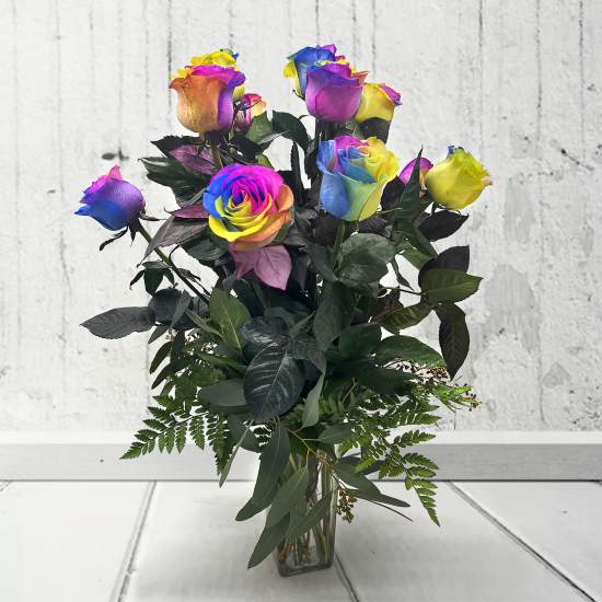 Rainbow-colored roses in a clear glass vase with dark foliage