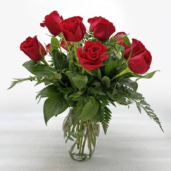 Red roses arranged in a clear glass vase with greenery