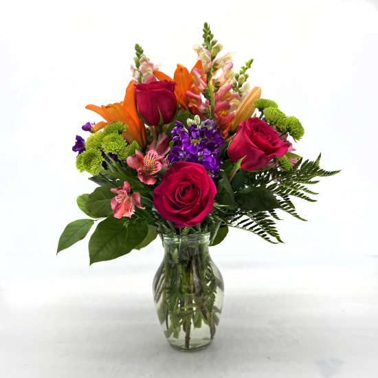 Mixed bouquet of roses, lilies, and purple flowers in a glass vase