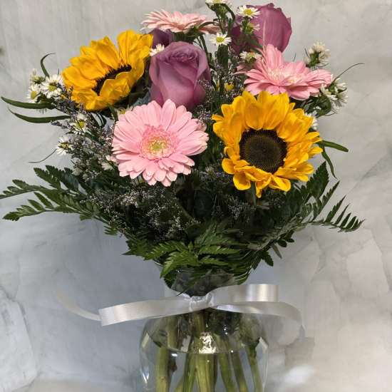 Mixed bouquet with sunflowers, pink gerberas, and a purple rose in a glass vase