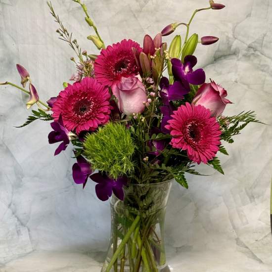 Pink gerberas, roses, and purple orchids in a clear glass vase