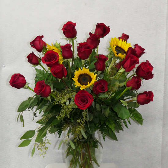 Red roses and sunflowers arranged in a clear glass vase