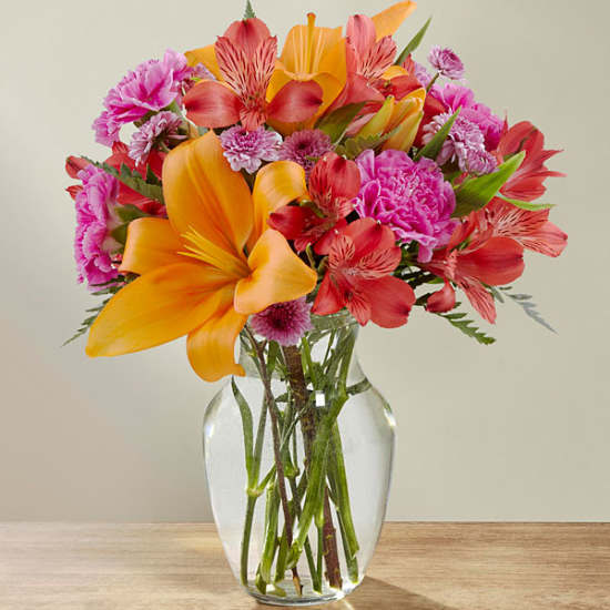 Bright mixed bouquet of orange, pink, and red flowers in a clear glass vase