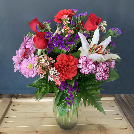 Mixed bouquet of red roses, lilies, carnations, and pink daisies in a glass vase