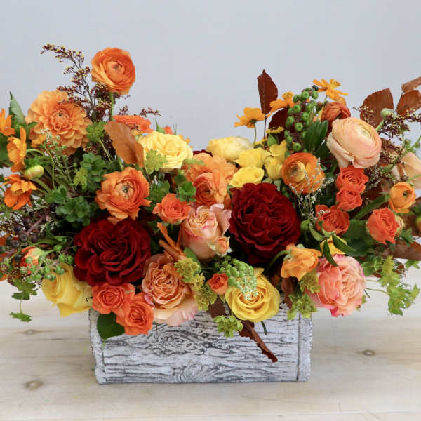 Low autumn-toned arrangement of orange, yellow, and red flowers in a whitewashed wooden box