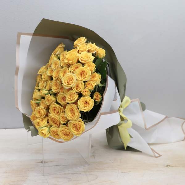 Large bouquet of clustered yellow roses wrapped in white and green paper with a bow