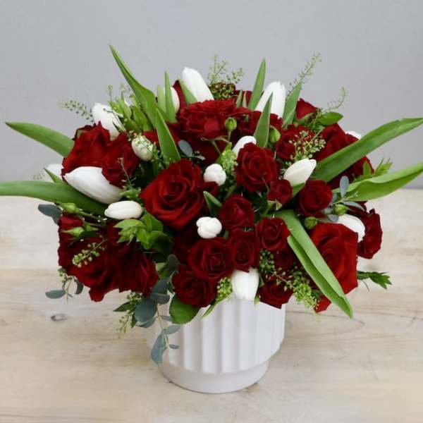 Low red rose and white tulip arrangement in a white ceramic vase