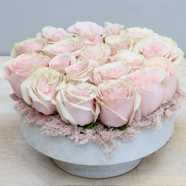 Low round arrangement of pale pink roses tightly packed in a white bowl