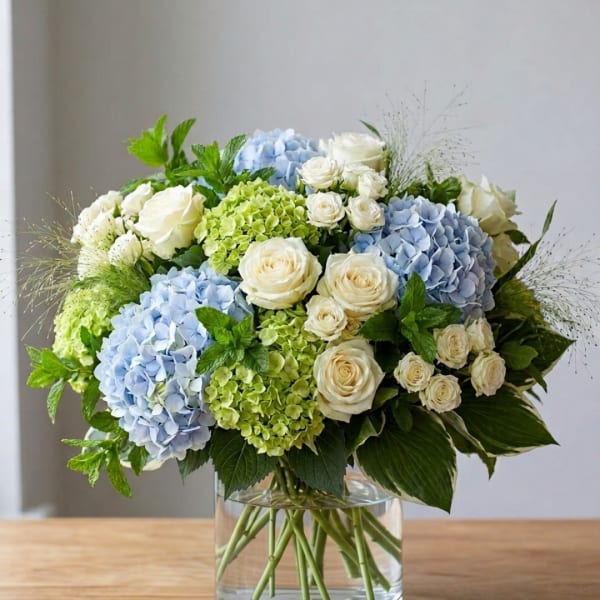 Blue and green hydrangea bouquet with white roses in a glass vase