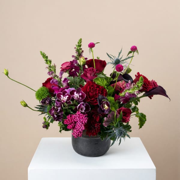 Mixed bouquet of red, pink, and purple flowers in a dark vase