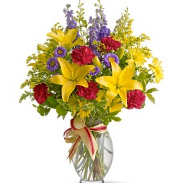 Bouquet of yellow lilies, red carnations, and purple flowers in a glass vase