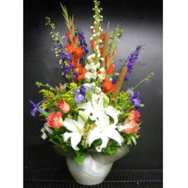 Tall mixed arrangement of white lilies, orange and purple flowers in a white vase