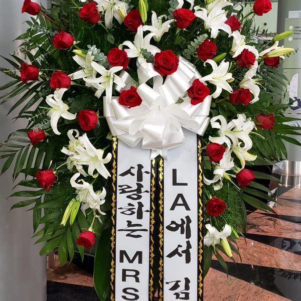 Large standing floral spray with red roses and white lilies, topped with a white bow