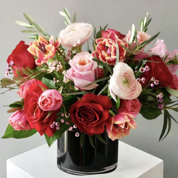 Bouquet of red and pink roses with pale ranunculus in a black vase