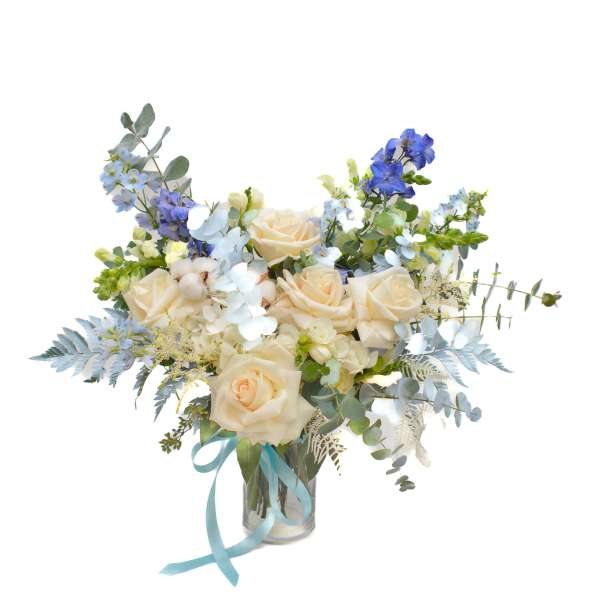Bouquet of cream roses and blue flowers in a glass vase