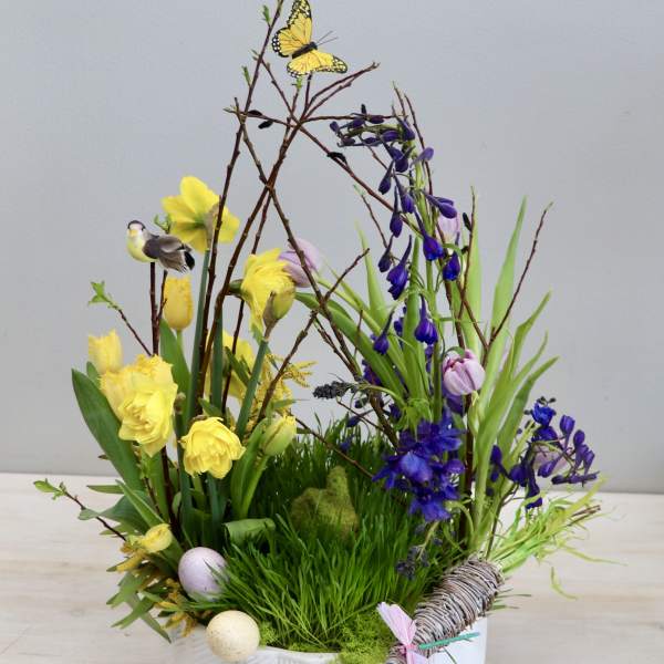 Low white bowl with yellow daffodils, purple flowers, grass and Easter accents like eggs, bird, and butterfly