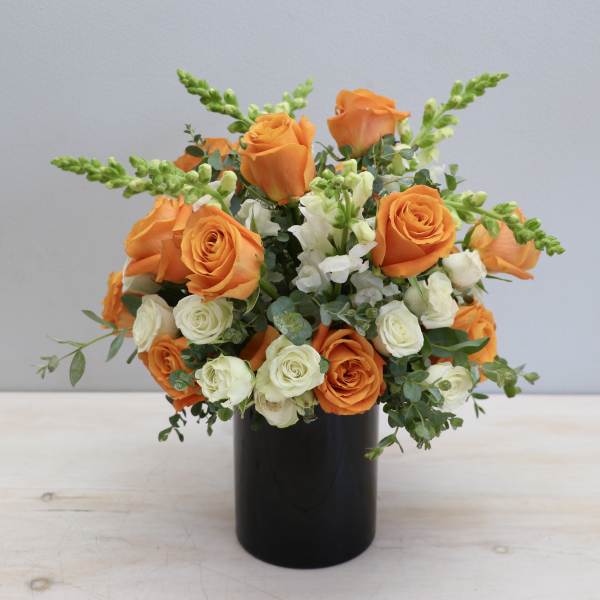 Orange and cream roses with white snapdragons in a black cylinder vase