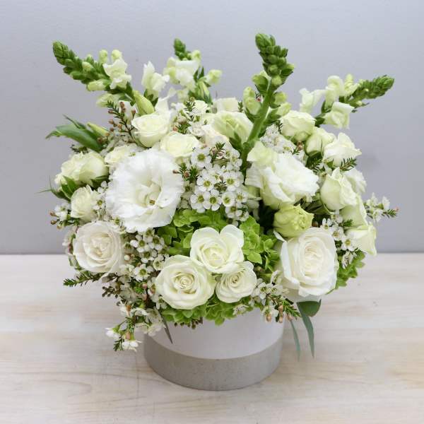 Round white flower arrangement with roses and snapdragons in a white ceramic vase