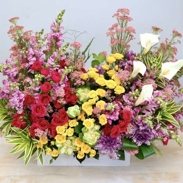 Large rectangular arrangement of bright pink, yellow, red, and white flowers in a white container