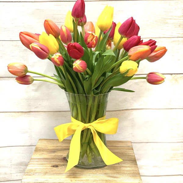 Mixed red, yellow, and orange tulips in a clear glass vase with a yellow ribbon bow.