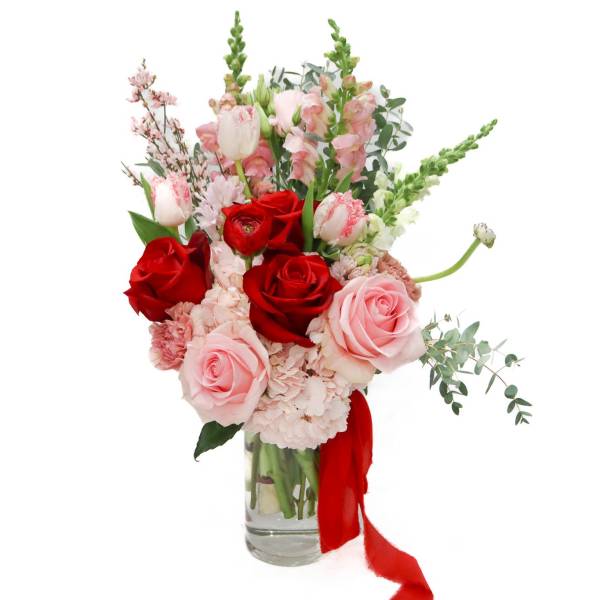 Red and pink roses in a clear glass vase with a red ribbon