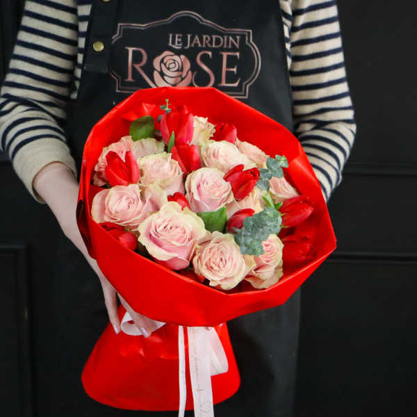 Bouquet of pale pink roses and red tulips wrapped in bright red paper