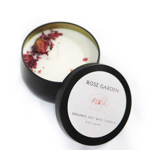 Black tin candle with rose petals on top and a matching lid beside it