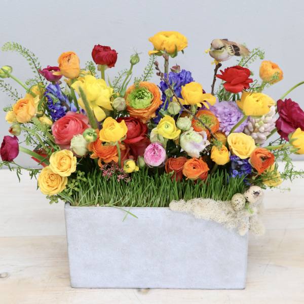 Low rectangular planter filled with bright multicolored spring flowers and grass.