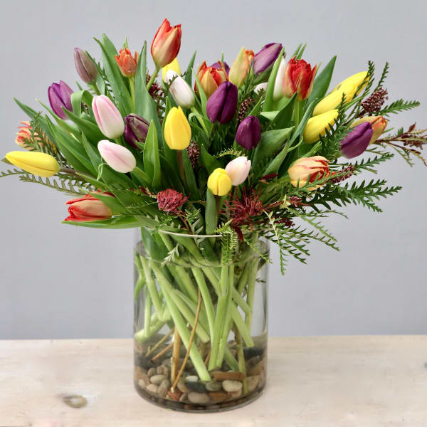 Tall clear glass vase of mixed-color tulips with river stones at the base
