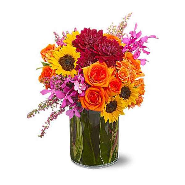 Bright mixed bouquet of roses, sunflowers, and mums in a glass vase