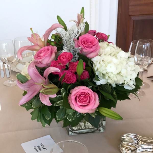 Pink roses and lilies arranged with white hydrangeas in a square glass vase