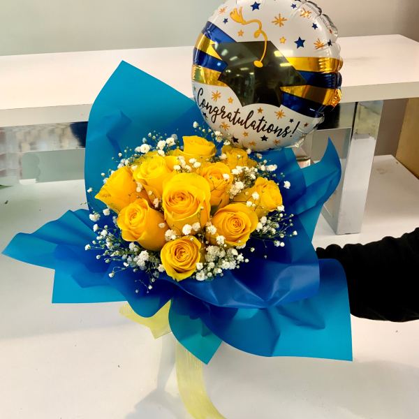 Bouquet of yellow roses with white filler flowers in blue wrap with a congratulations balloon
