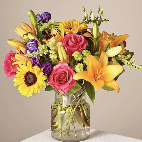 Mixed bouquet of roses, lilies, and sunflowers in a glass vase
