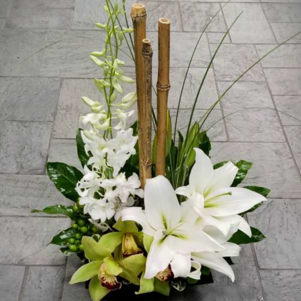 Modern arrangement of white lilies and orchids with bamboo in a low black container