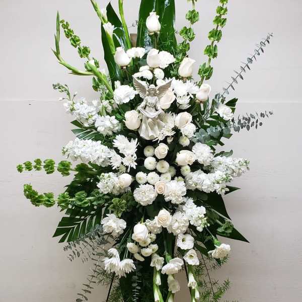 Tall white standing spray with roses, carnations, mums and an angel figurine on an easel