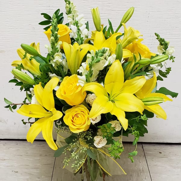 Yellow lilies and roses arranged in a clear glass vase